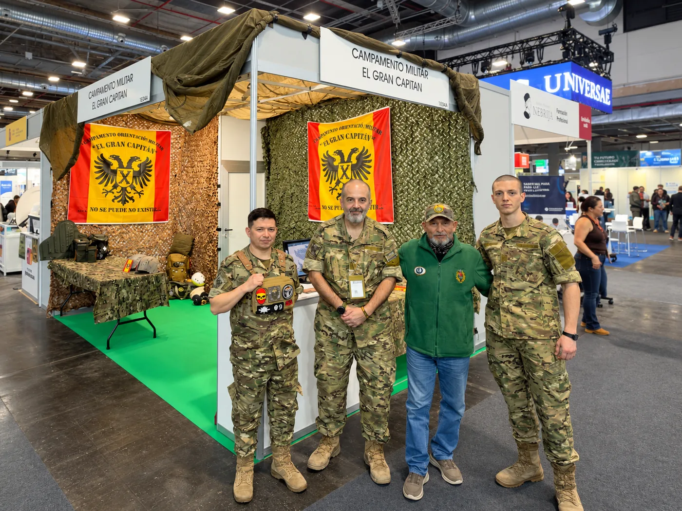 Stand del Campamento El Gran Capitán en IFEMA, con monitores atendiendo bajo las banderas del campamento